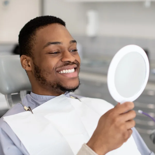 dentistry-adult man looking in mirror at his teeth in a dental office
