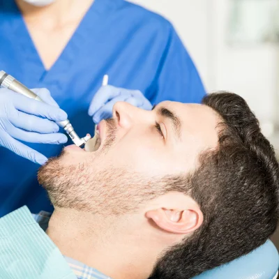 teeth-polishing adult man having his teeth polished by a female hygienist in clinic