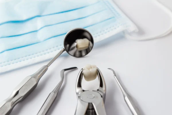 Dental extraction tools holding a tooth next to a mask